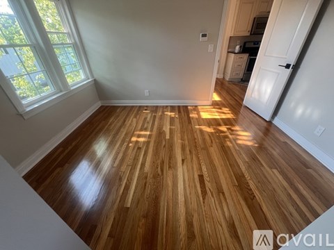 A room with wooden flooring and a window letting in sunlight.