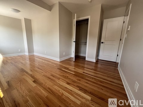 A room with wooden flooring and white walls, with a door in the background.