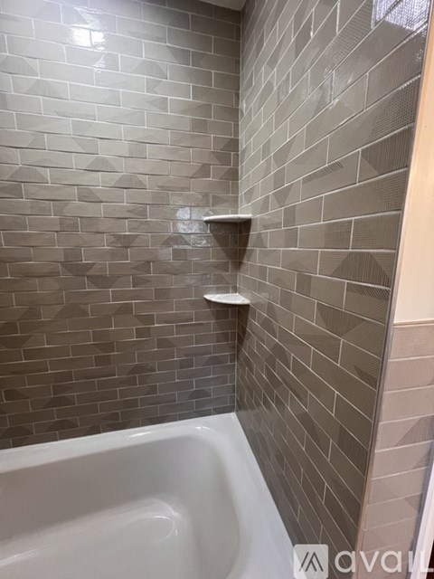A bathroom with a white tub and grey tiled walls.