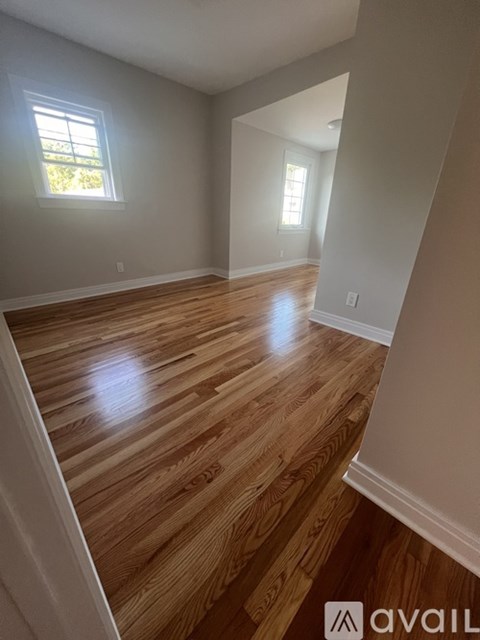A room with wooden flooring and two windows.