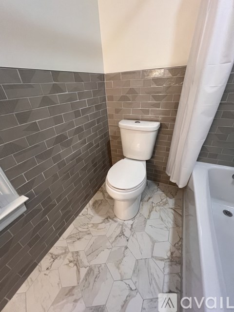 A white toilet in a bathroom with grey tiled walls.