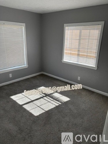 A room with grey walls and carpet, two windows with blinds, and a watermark that reads "SeniorRealEstate.com".