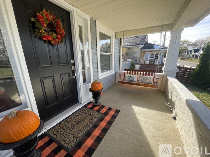 A black door with a wreath and two pumpkins on a porch.