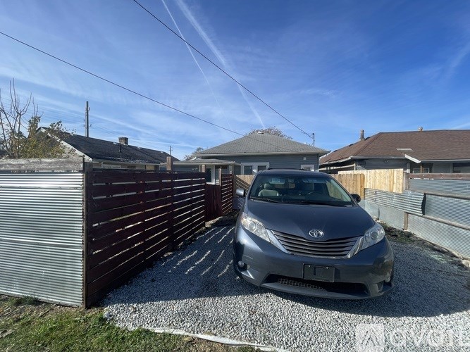 A grey car is parked in a gravel driveway.