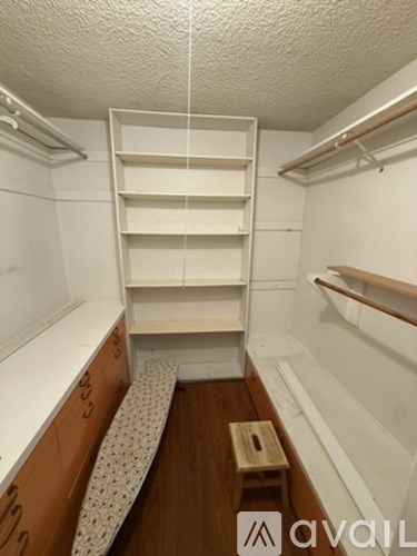 A small, white, padded bench sits under a shelf in a small room.