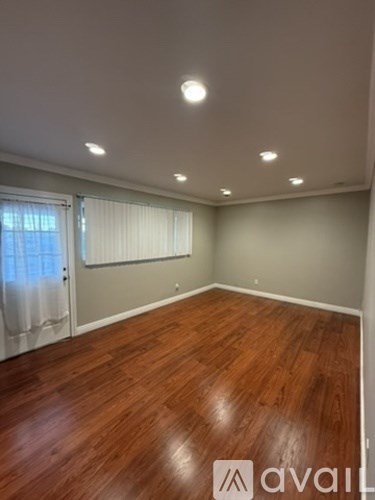 A room with wooden flooring and a window with curtains.