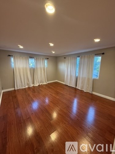 A room with wooden flooring and white curtains.
