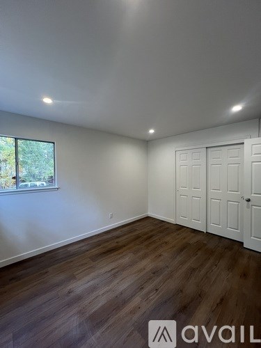 A room with wooden floors and white walls, with a window and a door.