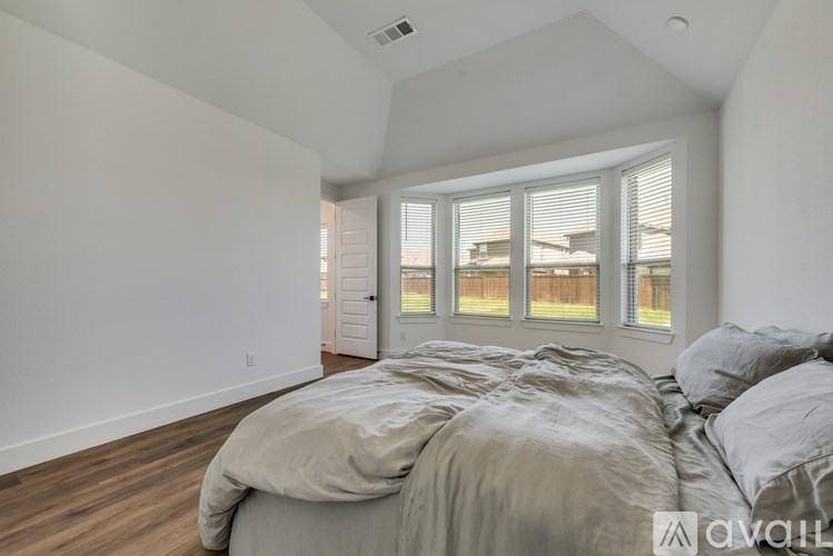 A bedroom with a large bed and a view of a house through the window.