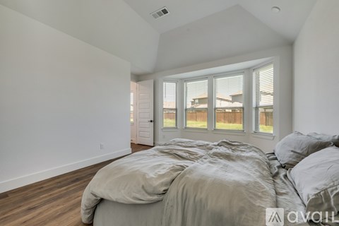 A bedroom with a large bed and a view of a house through the window.