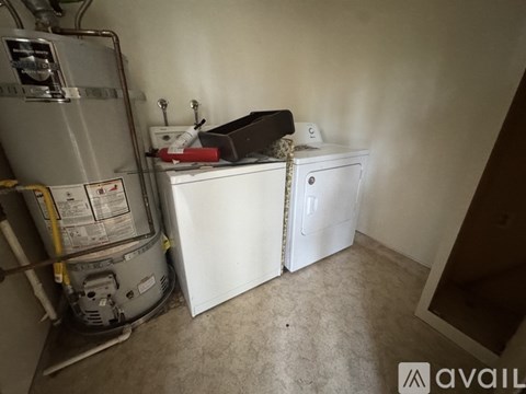 A room with a white refrigerator and a white washing machine with a black box on top of the washing machine.