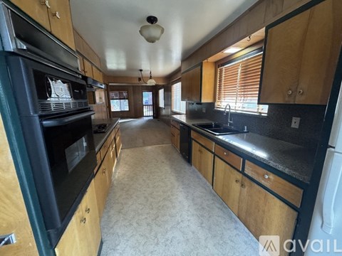 A kitchen with wooden cabinets and black appliances is available for rent.