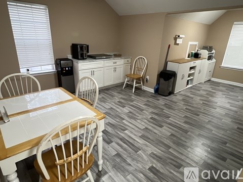 A kitchen with a table and chairs in the foreground and a counter with a coffee maker in the background.