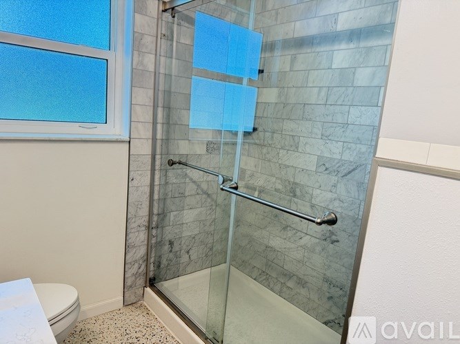 A bathroom with a glass shower enclosure and a toilet.