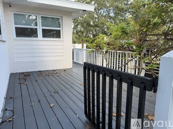 A wooden deck with a black railing and a white house in the background.