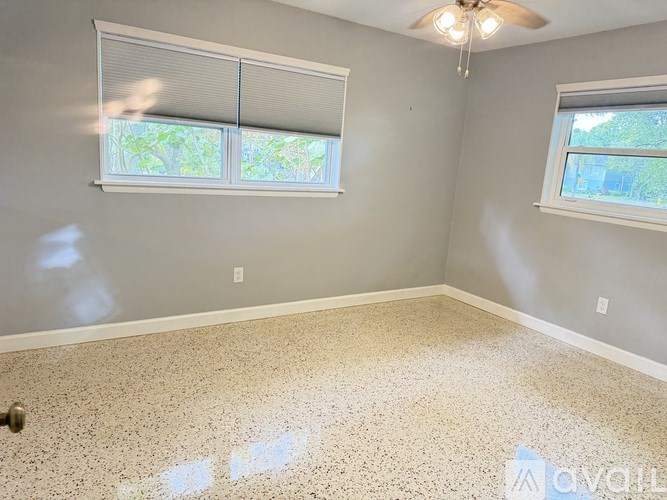 A room with a ceiling fan and two windows.