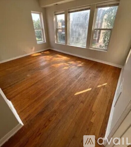 A room with wooden flooring and three windows.
