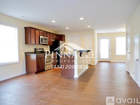 A spacious living room with wood flooring and a kitchen area with brown cabinets and appliances.