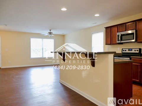 A spacious living room with a kitchen area and a ceiling fan.