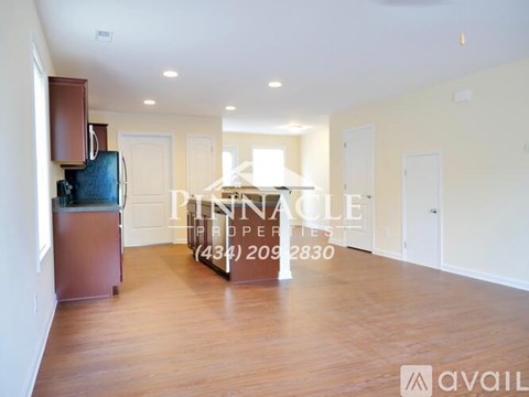 A spacious living room with wood flooring and a kitchen area in the background.