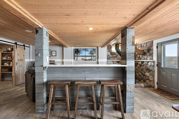 A modern kitchen with a stone fireplace and wooden stools.