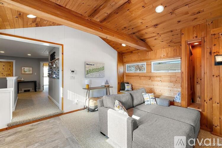 A living room with a grey couch and wooden walls.