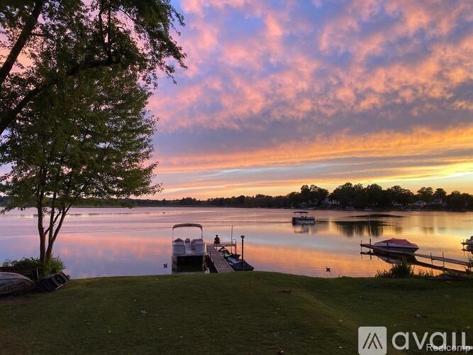 A serene lakeside scene with boats docked at a pier and a tree in the foreground.