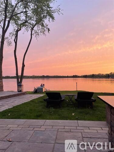 Two black chairs are placed on the grass by the water.