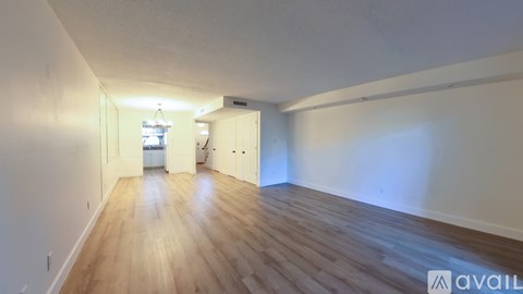 A room with wooden flooring and white walls, with a doorway leading to another room.