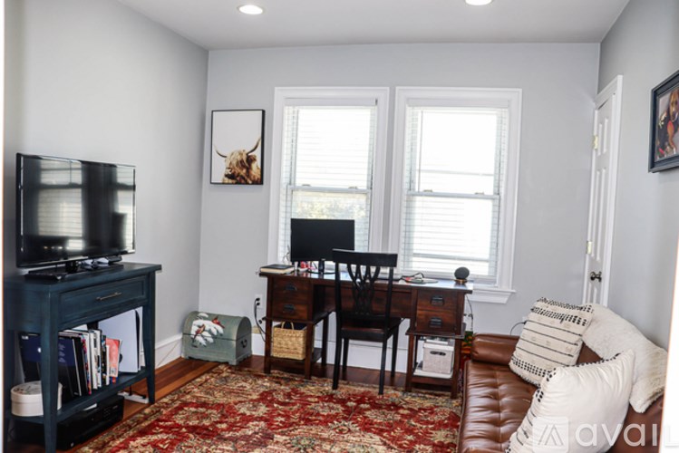 A living room with a brown leather couch, a wooden desk, and a television.