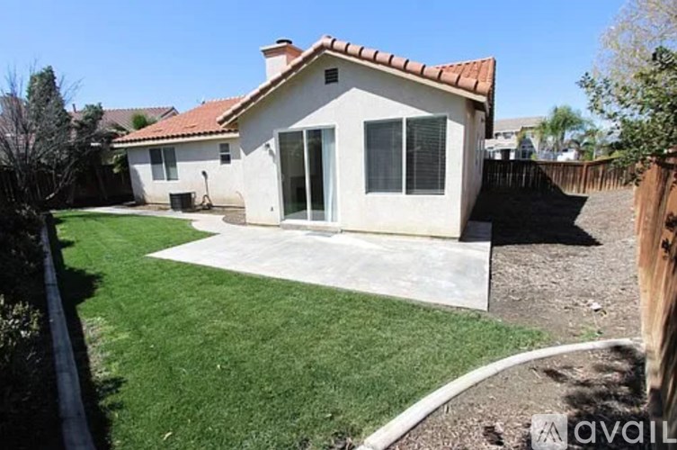 A house with a red tile roof and a white exterior is surrounded by a green lawn.
