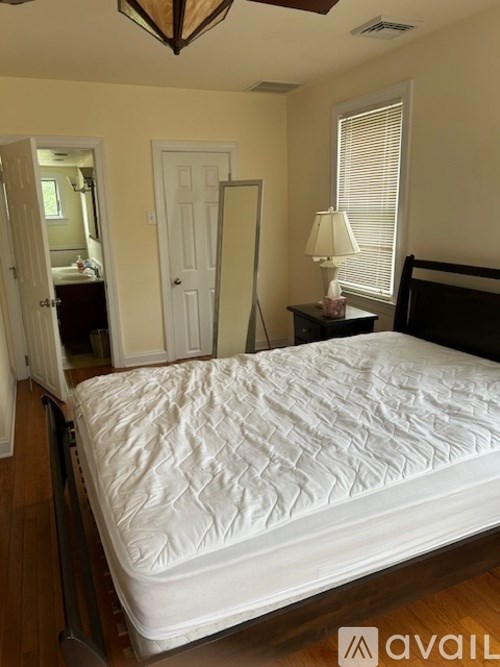 A bed with a white mattress is in the middle of a room with a lamp and a door.