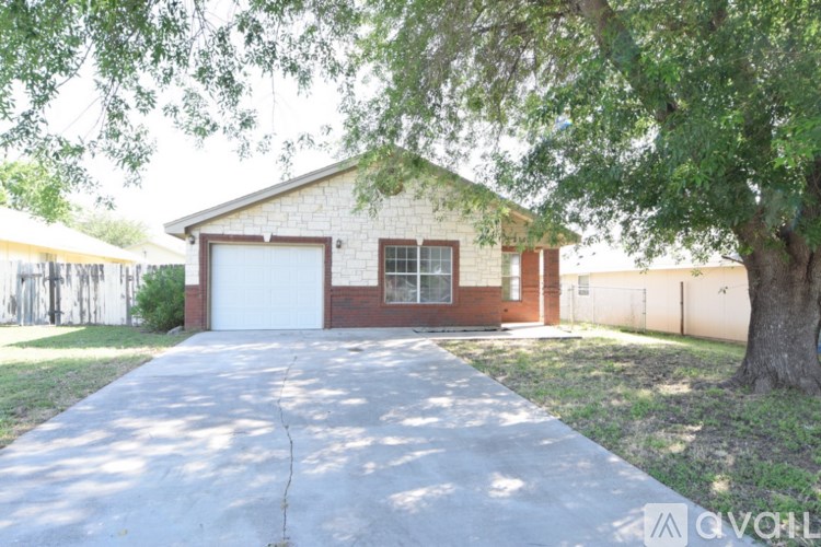 A house with a garage and a driveway is surrounded by a fence and a tree.