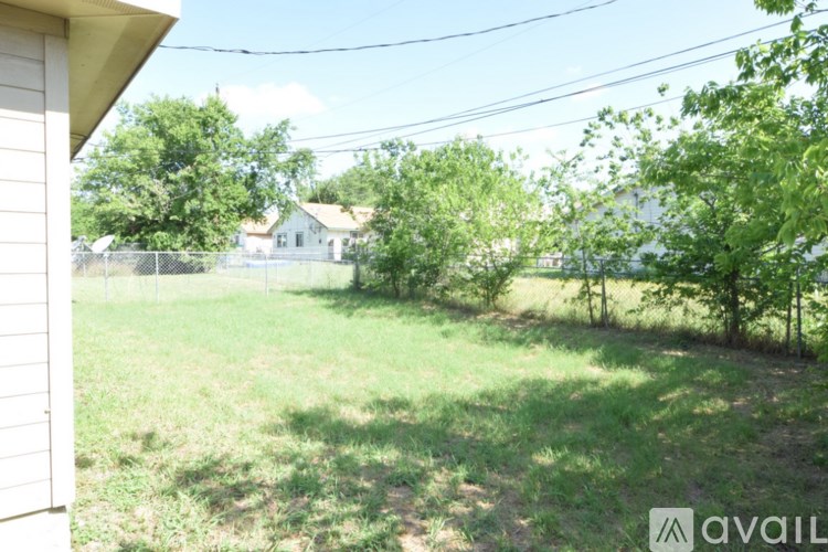 A grassy backyard with a house and trees in the background.