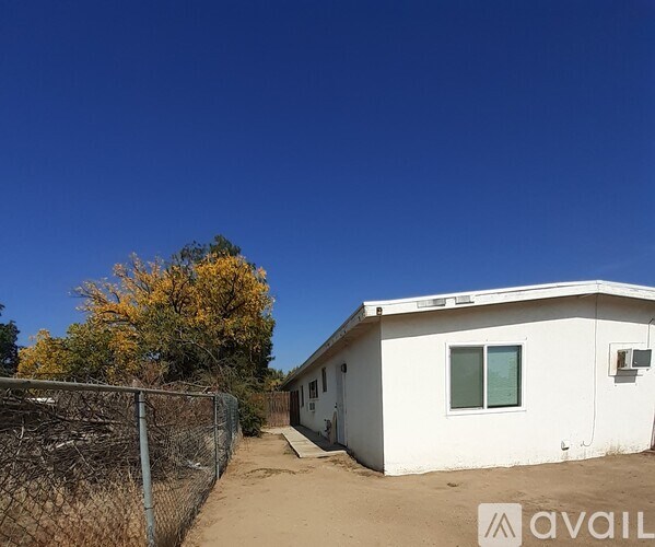 A white house with a fence and a tree with yellow leaves in the background.