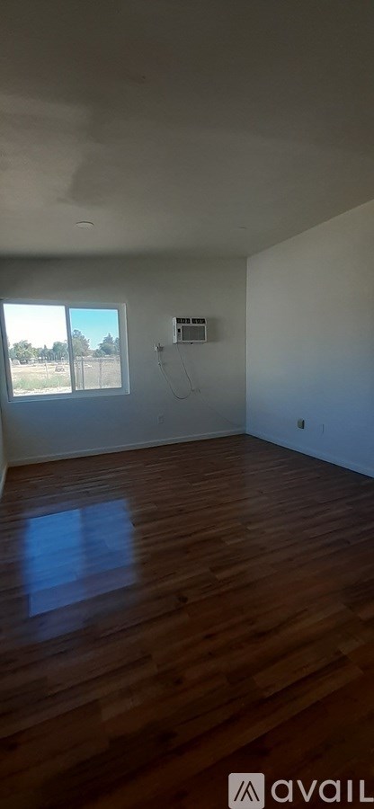 A room with wooden flooring and a window overlooking a field.