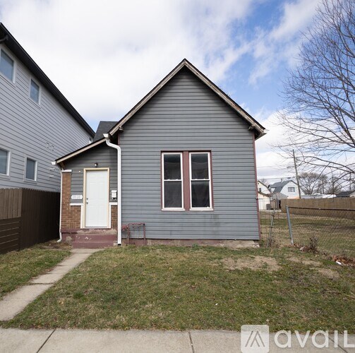 A small house with a grey siding and a white door is for sale.