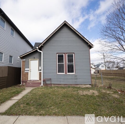 A small house with a grey siding and a white door is for sale.