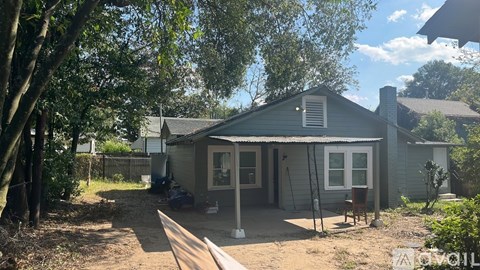 A house with a grey roof and a white door is surrounded by trees.