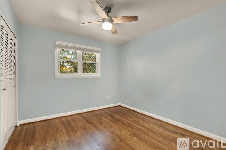 A room with a ceiling fan and a window with a view of trees.