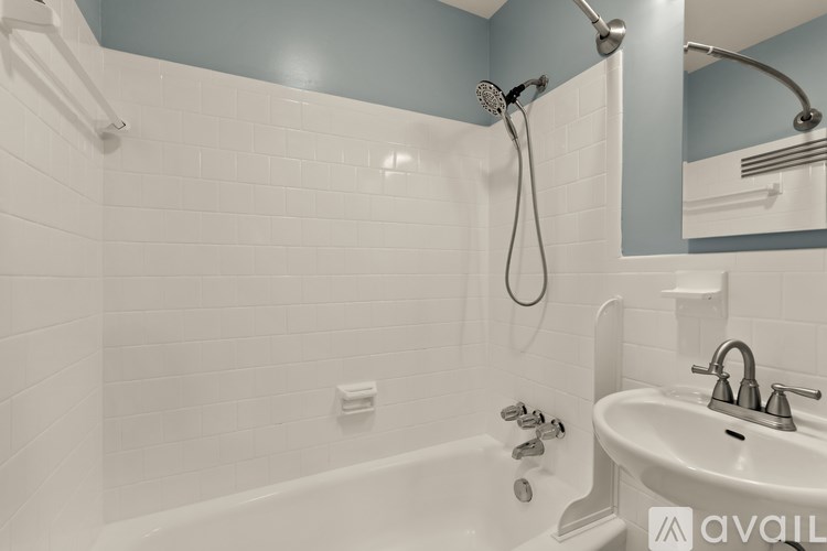 A white bathtub with a shower head and a white sink with a silver faucet.