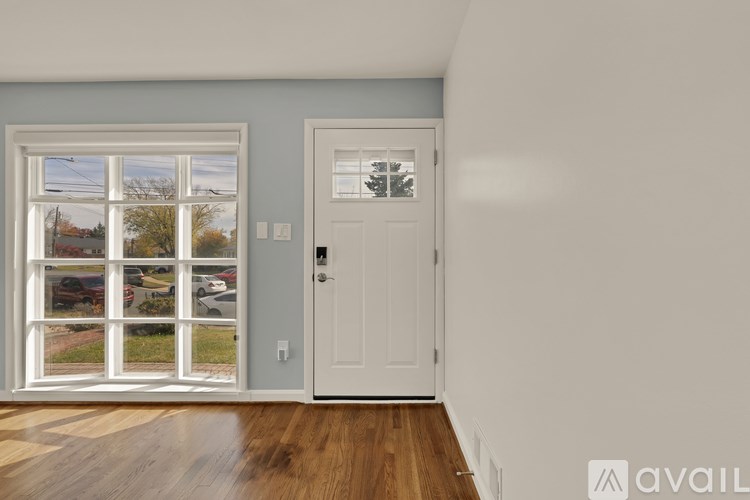 A room with a white door and a window showing a view of cars and trees.