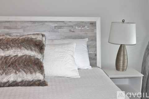A bed with a grey headboard and a white pillow is in front of a grey wall.