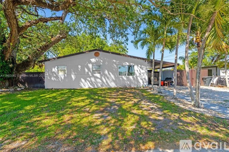 A house with a white exterior is surrounded by greenery and trees.