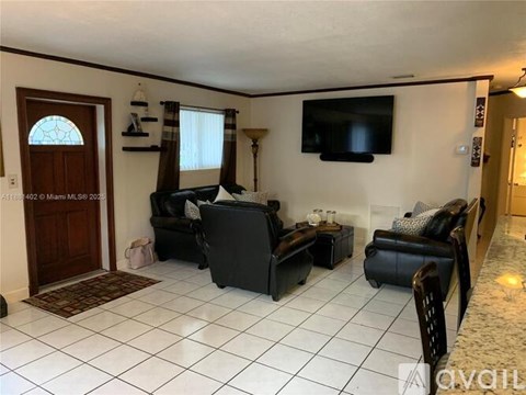 A living room with a black sofa set and a flat screen TV mounted on the wall.