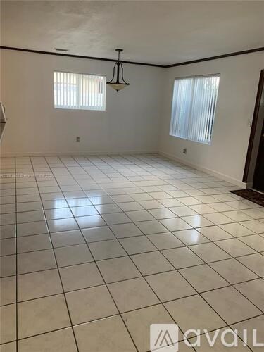 A large empty room with white tiled flooring and two windows.