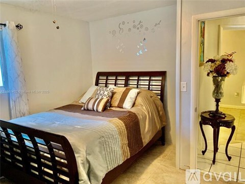 A bedroom with a bed, a chair, and a table with a vase of flowers.