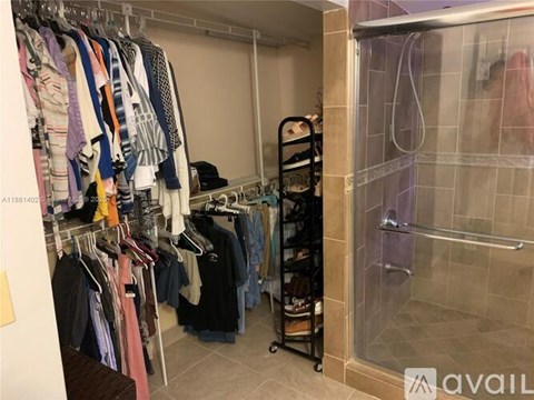 A walk in closet with clothes hanging and a glass shower door.