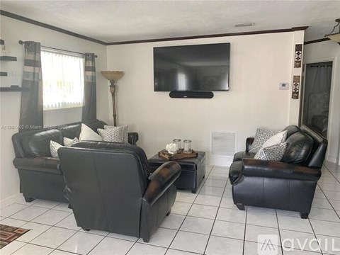 A living room with two black leather couches and a television mounted on the wall.