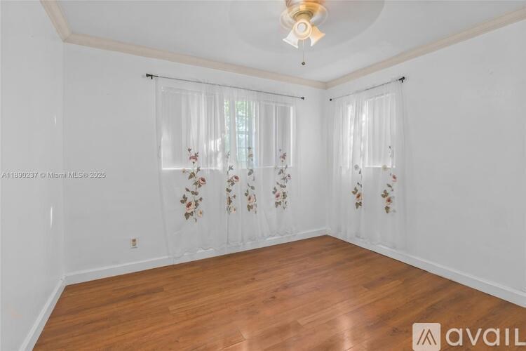 A room with wooden floors and white walls, featuring a window with curtains and a ceiling light fixture.